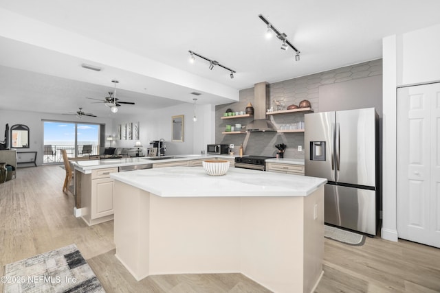 kitchen featuring stainless steel appliances, backsplash, kitchen peninsula, a kitchen island, and light wood-type flooring