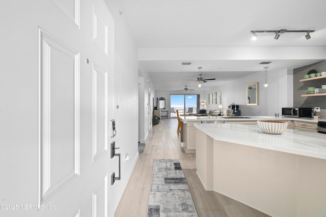 kitchen with ceiling fan, light stone countertops, hanging light fixtures, and light hardwood / wood-style flooring