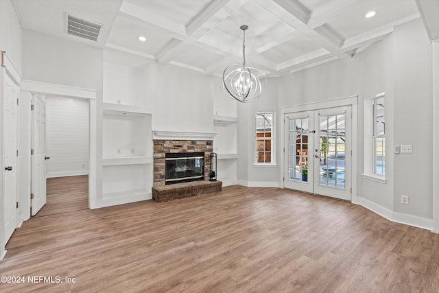 unfurnished living room with beam ceiling, light wood-type flooring, a fireplace, french doors, and coffered ceiling