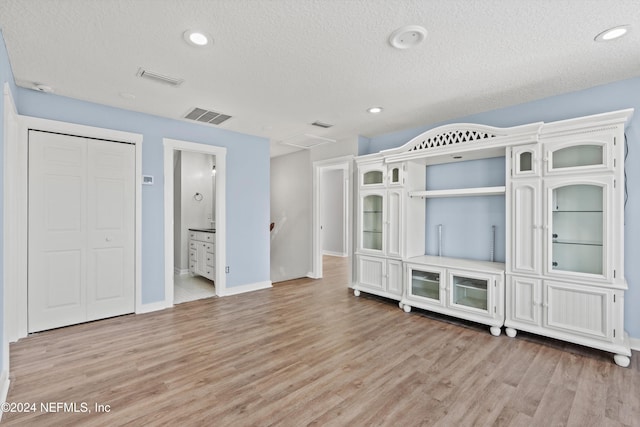 unfurnished bedroom featuring a closet, light hardwood / wood-style flooring, a textured ceiling, and ensuite bathroom