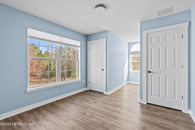 unfurnished bedroom featuring multiple windows, hardwood / wood-style floors, and a textured ceiling