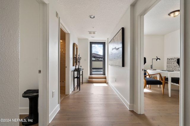 hall featuring light wood-type flooring and a textured ceiling