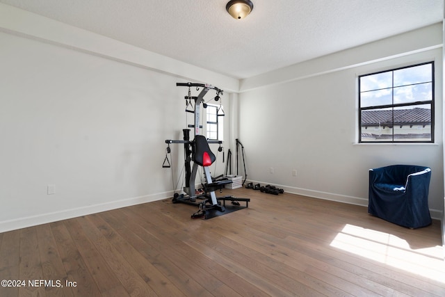 workout room with wood-type flooring, a textured ceiling, and baseboards