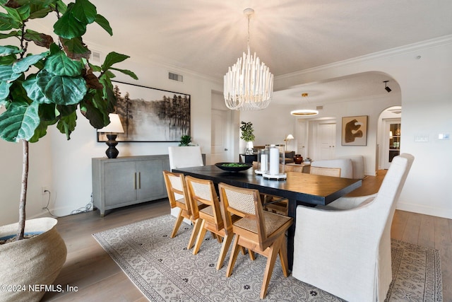 dining space with arched walkways, ornamental molding, wood finished floors, and visible vents