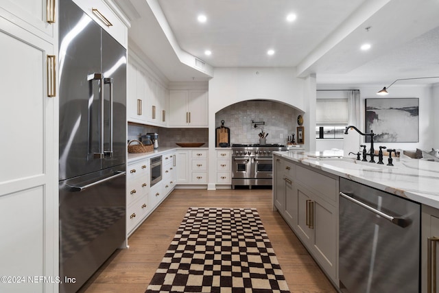 kitchen with hardwood / wood-style flooring, custom range hood, sink, gray cabinets, and built in appliances