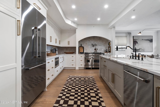 kitchen featuring decorative backsplash, premium appliances, light stone countertops, white cabinetry, and a sink