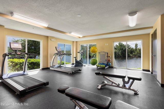 gym with a healthy amount of sunlight, baseboards, and a textured ceiling