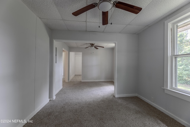 carpeted empty room featuring plenty of natural light, ceiling fan, and a drop ceiling