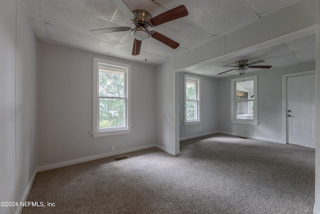 carpeted spare room featuring a healthy amount of sunlight, a paneled ceiling, and ceiling fan