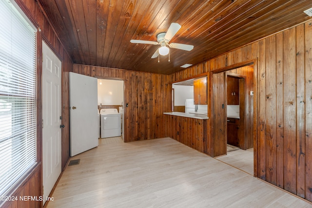 spare room with washer / clothes dryer, ceiling fan, wood walls, and light wood-type flooring