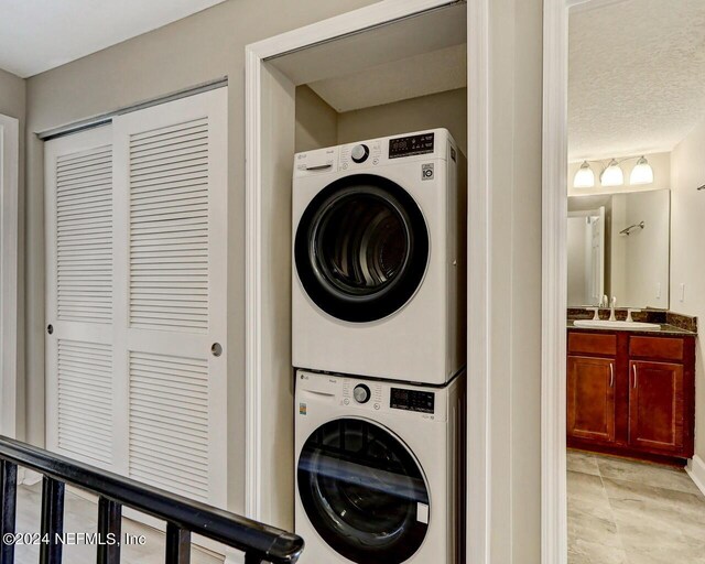 clothes washing area with a textured ceiling, sink, and stacked washer and dryer