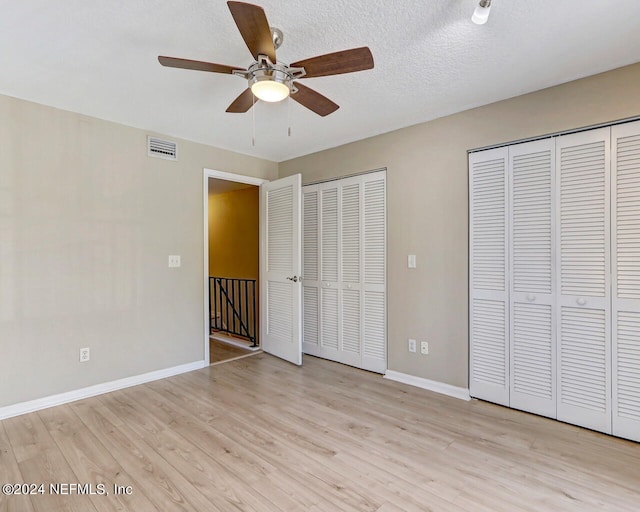 unfurnished bedroom featuring light wood-type flooring, ceiling fan, a textured ceiling, and multiple closets