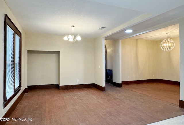 empty room featuring a textured ceiling, a notable chandelier, and hardwood / wood-style floors