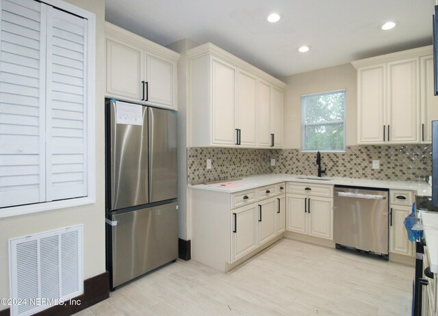 kitchen with light wood-type flooring, appliances with stainless steel finishes, backsplash, and sink