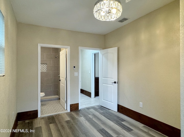 unfurnished bedroom with ensuite bath, a chandelier, and hardwood / wood-style flooring