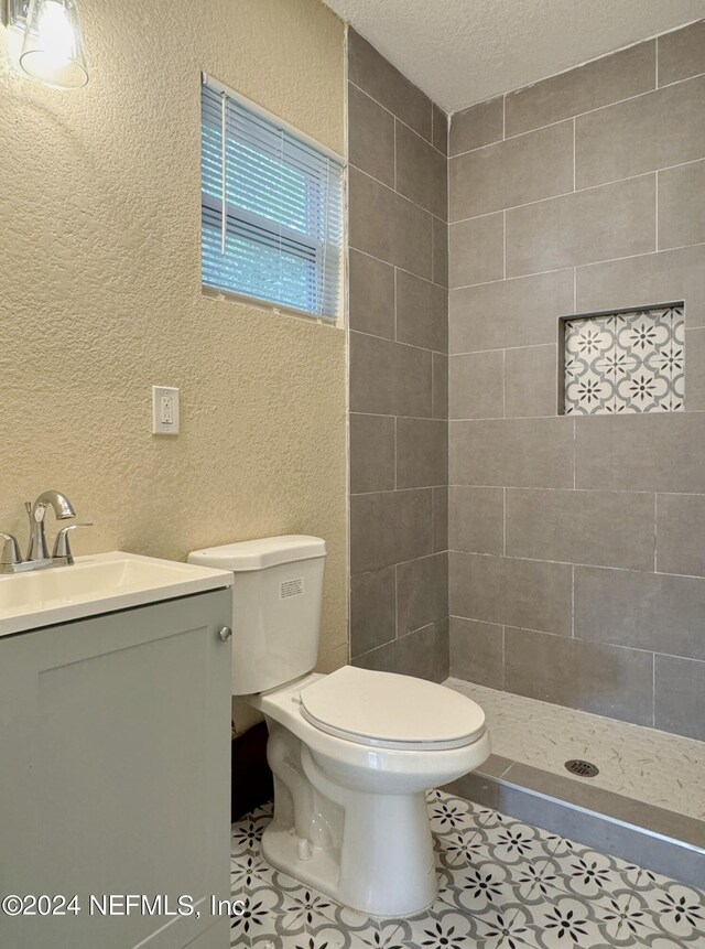 bathroom with tile patterned floors, tiled shower, toilet, and vanity