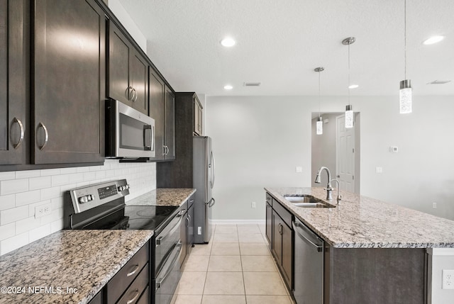 kitchen featuring tasteful backsplash, appliances with stainless steel finishes, a kitchen island with sink, sink, and decorative light fixtures