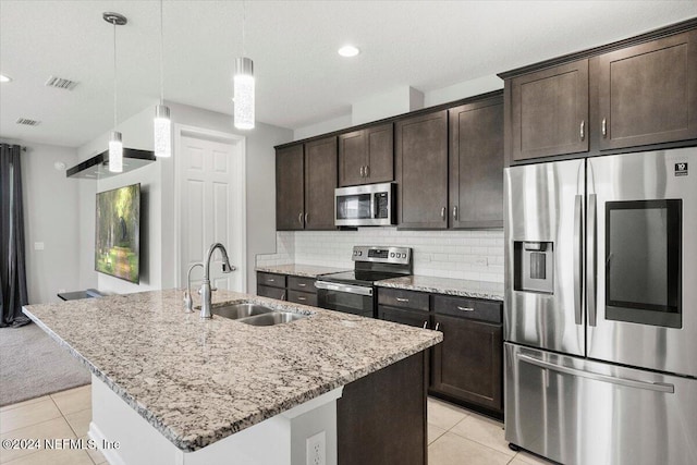 kitchen with light stone countertops, a kitchen island with sink, stainless steel appliances, sink, and decorative light fixtures