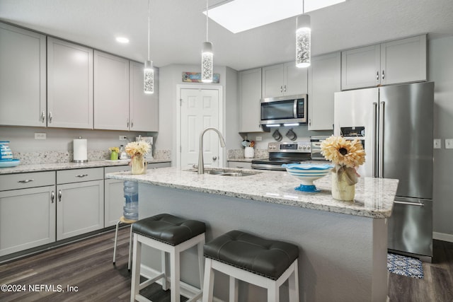 kitchen featuring dark wood-style flooring, stainless steel appliances, gray cabinetry, a sink, and a kitchen breakfast bar