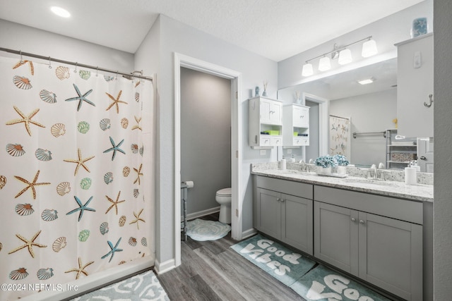 full bathroom with curtained shower, toilet, wood finished floors, a sink, and double vanity