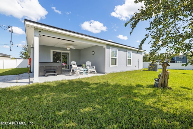 back of property with fence, a ceiling fan, a lawn, a patio area, and a hot tub