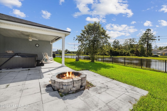 view of patio featuring a water view, a hot tub, a ceiling fan, a fenced backyard, and a fire pit