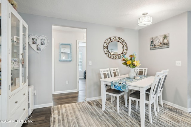 dining space featuring dark wood-style floors, a textured ceiling, and baseboards