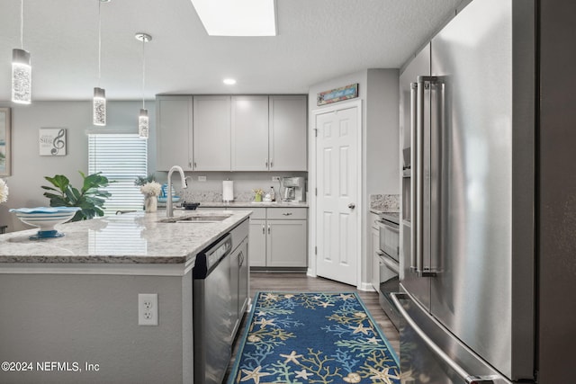 kitchen featuring light stone counters, stainless steel appliances, dark wood-type flooring, a sink, and decorative light fixtures