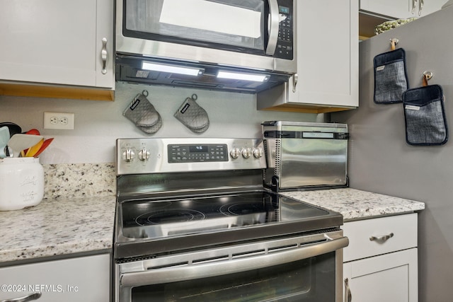 kitchen with light stone countertops, white cabinetry, and appliances with stainless steel finishes