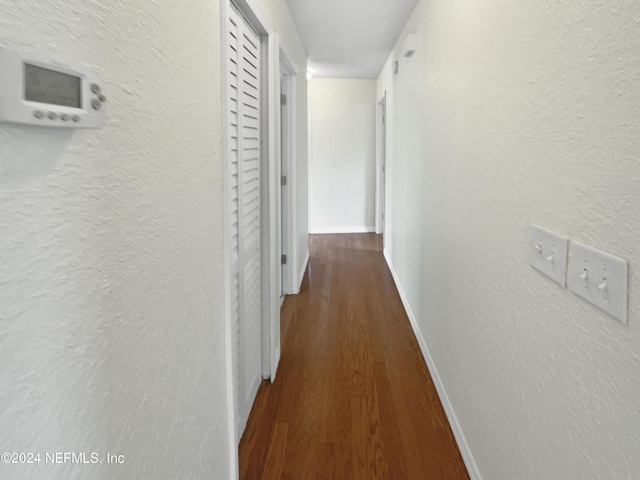 hallway featuring dark wood-style floors, a textured wall, and baseboards