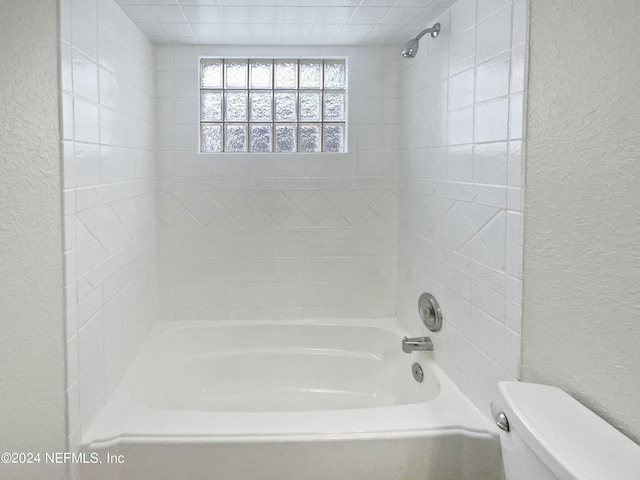 bathroom featuring a textured wall, bathing tub / shower combination, and toilet