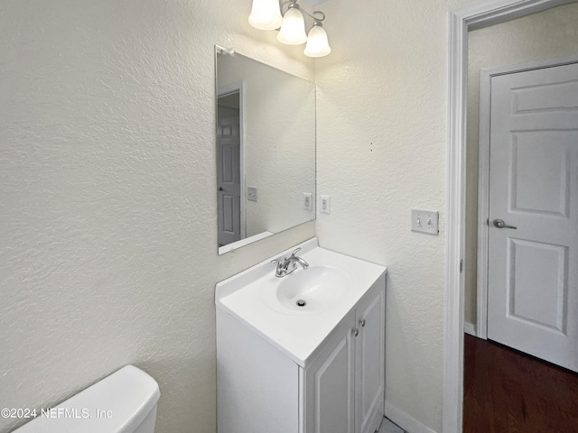 half bath with a textured wall, vanity, and toilet