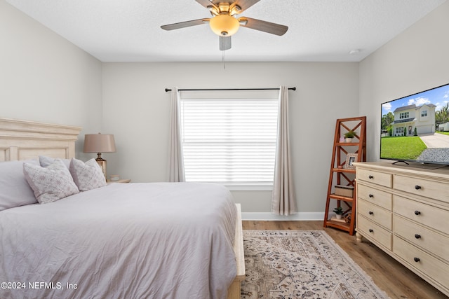 bedroom featuring a textured ceiling, a ceiling fan, light wood-style flooring, and baseboards