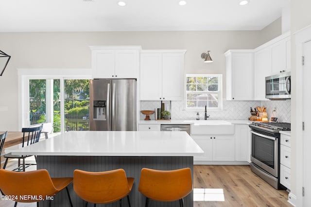 kitchen with a breakfast bar area, backsplash, appliances with stainless steel finishes, white cabinets, and a sink