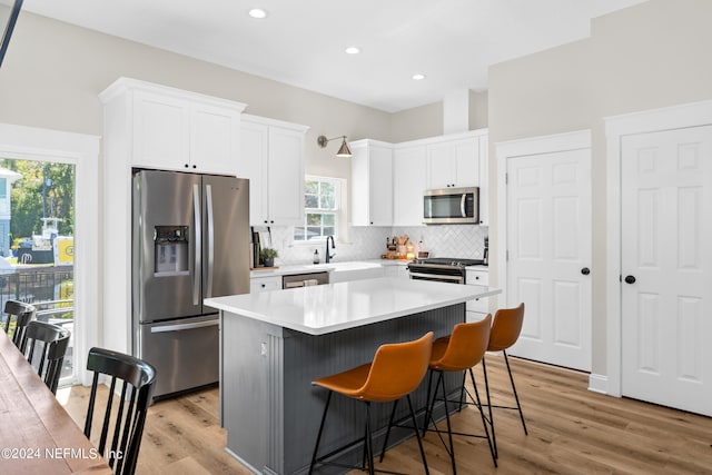 kitchen with tasteful backsplash, appliances with stainless steel finishes, light wood-style floors, and white cabinets