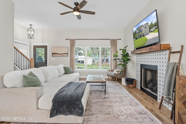 living room with ceiling fan with notable chandelier, a fireplace, wood finished floors, and stairs