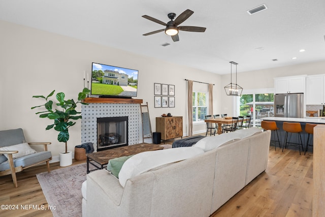 living area featuring light wood-type flooring, a ceiling fan, visible vents, and a tiled fireplace