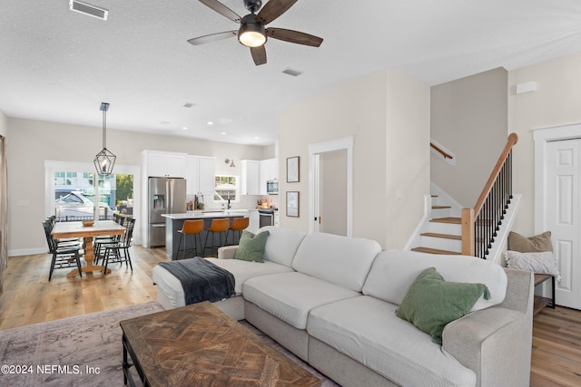 living area with a textured ceiling, visible vents, a ceiling fan, stairs, and light wood-type flooring