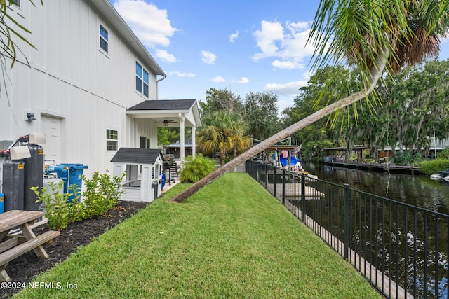 view of yard featuring a water view, fence, and ceiling fan