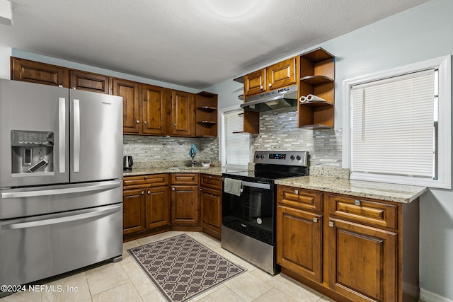 kitchen with light tile patterned floors, appliances with stainless steel finishes, light stone counters, and decorative backsplash