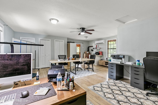 office space with a wall mounted AC, a textured ceiling, ceiling fan, and light hardwood / wood-style floors