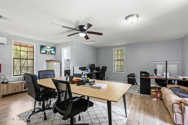 office space with light hardwood / wood-style flooring, ceiling fan, and an AC wall unit