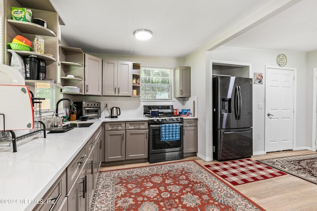 kitchen featuring stainless steel appliances, sink, light stone countertops, gray cabinetry, and light hardwood / wood-style floors