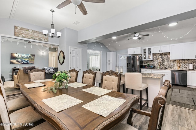 dining space with vaulted ceiling, ceiling fan with notable chandelier, and wood-type flooring