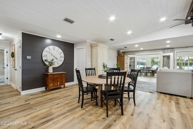 dining room featuring ornamental molding, light hardwood / wood-style flooring, wood walls, ceiling fan, and lofted ceiling