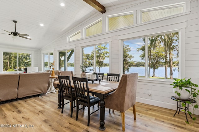 dining space with wood walls, beamed ceiling, ceiling fan, light wood-type flooring, and a water view