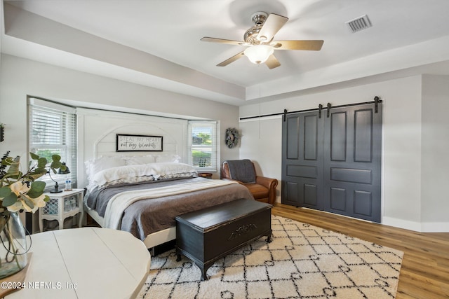 bedroom featuring light hardwood / wood-style flooring, ceiling fan, a barn door, and a closet