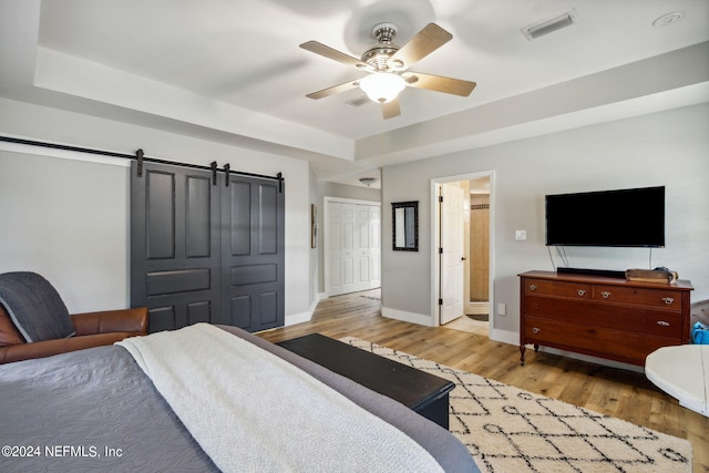 bedroom with a barn door, ceiling fan, a closet, and light hardwood / wood-style floors