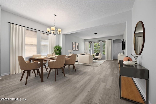 dining space with light wood-type flooring, a textured ceiling, and a notable chandelier