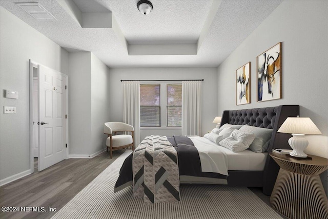 bedroom featuring dark wood-type flooring, a textured ceiling, and a raised ceiling